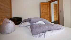 Ein Schlafzimmer mit einem Bett, zwei Kissen, einem Sessel und einer Holztür.