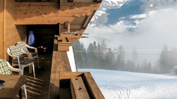 Une terrasse en bois avec une table et des chaises, offrant une vue sur un paysage montagneux enneigé.