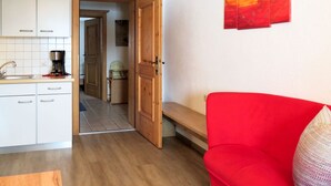 Un espace de vie compact comprenant un coin cuisine, un canapé rouge et une porte donnant sur un couloir.