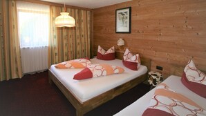 Habitación con paneles de madera, una cama, una ventana con cortinas, un cuadro colgado en la pared y una pequeña mesa con un objeto estampado con motivos de vaca.