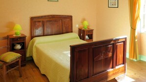 A bedroom with a wooden bed, a nightstand with a lamp, a chair, and a small table with a lamp.
