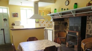 A cozy kitchen with a dining table, chairs, a fireplace, and a clock on the wall.