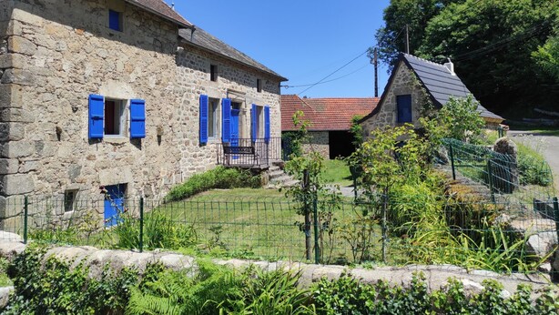 A stone building with blue shutters, a stone fence, and greenery.