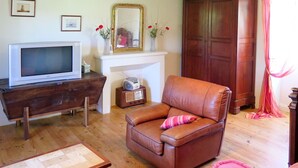 A living room with a brown leather sofa, a wooden coffee table, a white fireplace, a television, and a radio.