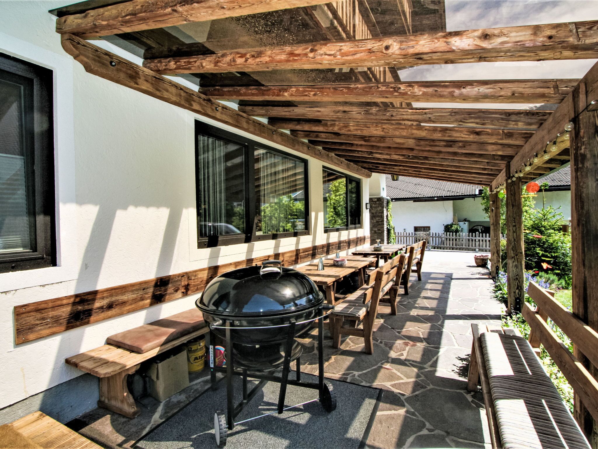 Une terrasse extérieure avec un barbecue, des bancs en bois et un sol en pierre.