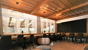 Un espace de restauration moderne avec des tables et des chaises en bois, de grandes fenêtres ornées de rideaux légers et des luminaires suspendus.