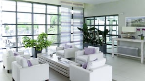 Un salon moderne avec des canapés blancs, une table basse et de grandes fenêtres donnant sur l’extérieur.