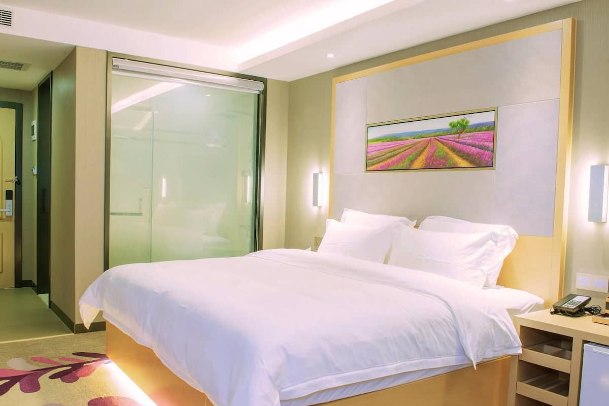Habitación de hotel con una cama grande, una puerta de cristal, un cuadro en la pared y un escritorio con un teléfono.