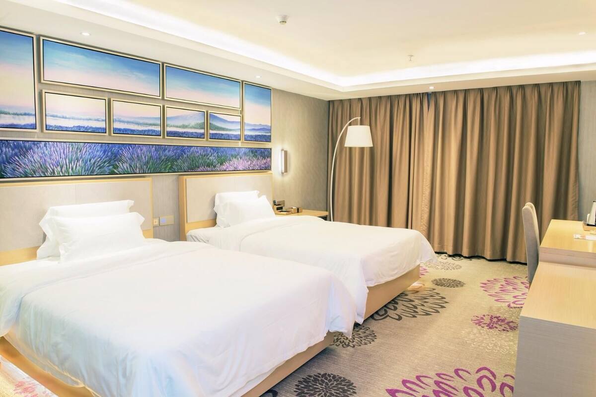 Una habitación de hotel con dos camas, un ventanal con vistas, un escritorio y una lámpara.