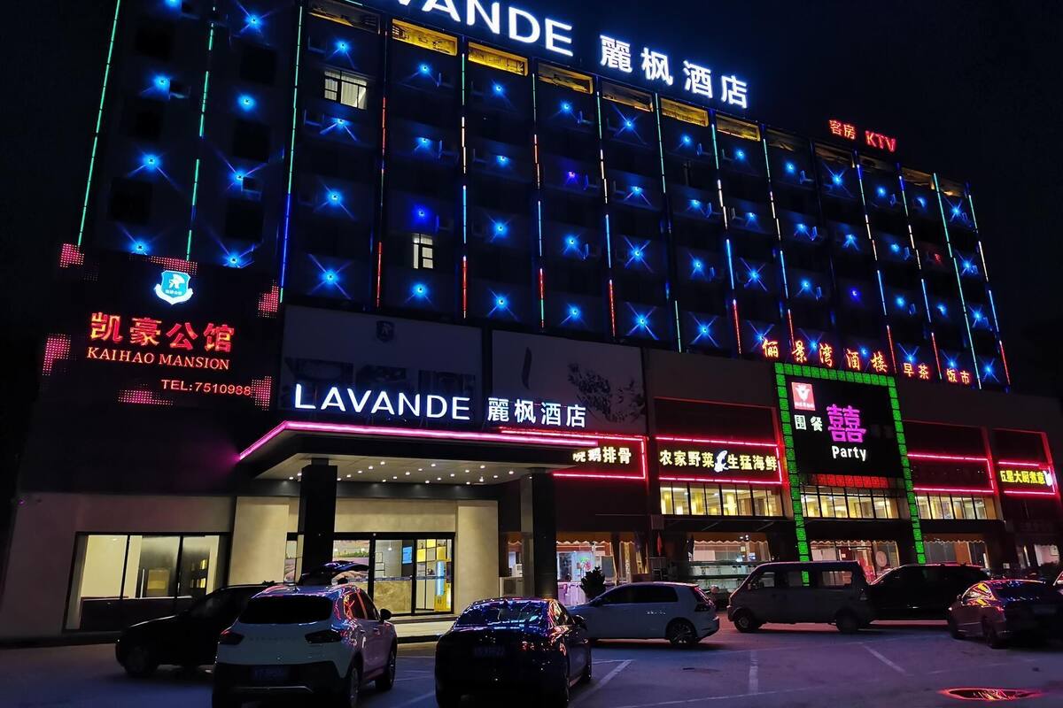 Un hotel con un llamativo letrero 'LAVANDE', varios pisos y un estacionamiento con varios coches.