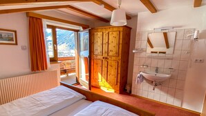 A bedroom with a bed, a wooden wardrobe, a bathroom with a sink, and a view of the outdoors. - Apartment Sonja by Interhome (Neustift im Stubaital)