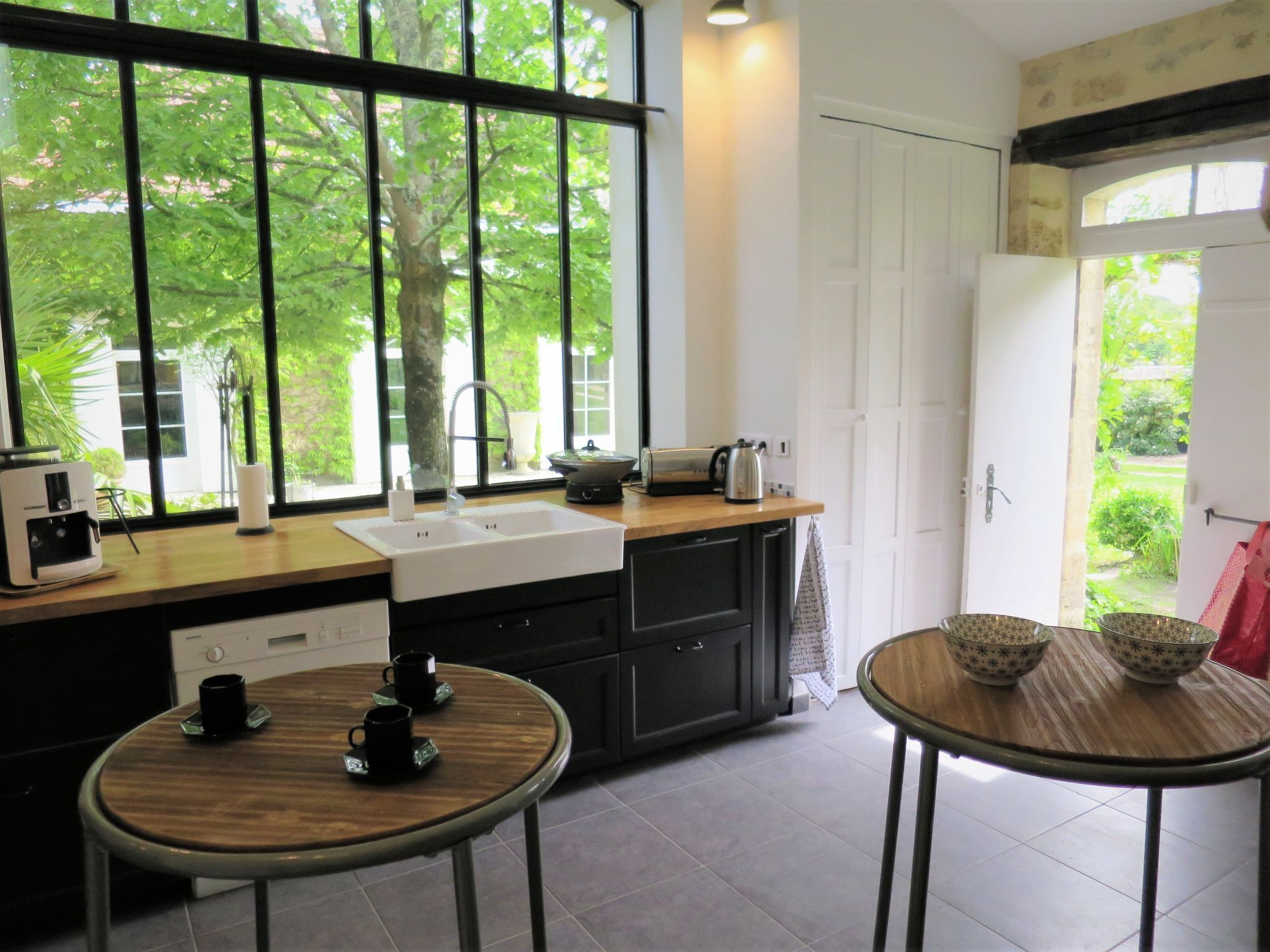 Eine moderne Küche mit einem großen Fenster, einer Spüle, einer Kaffeemaschine und einem kleinen Esstisch.