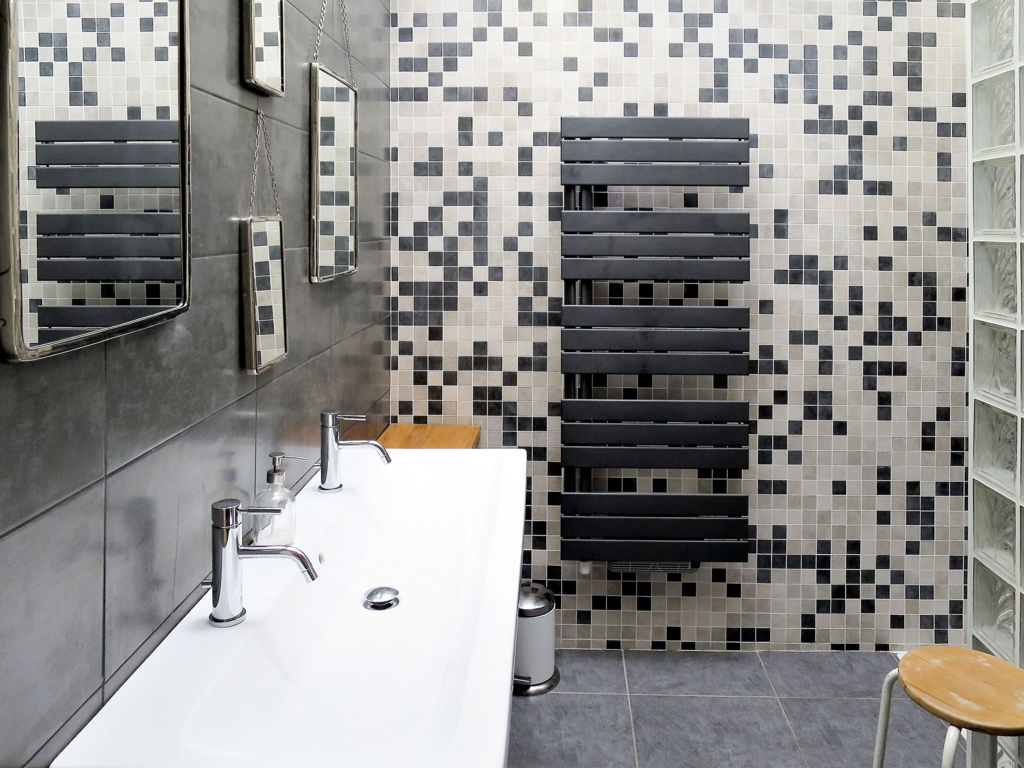 A modern bathroom with a white sink, chrome fixtures, a mirror, and a tiled wall with a pixelated pattern.