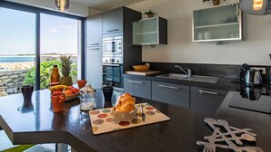 Cozinha moderna com ilha grande, eletrodomésticos embutidos e vista para a praia.