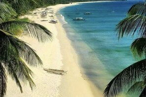 A beach with a sandy shore and palm trees. - Basios Place Tourist Inn by RedDoorz (Palawan)