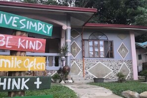 Une maison à la façade en pierre et au toit rouge. On peut y voir des panneaux colorés avec des messages tels que « VIVEZ SIMPLEMENT » et « SOYEZ GENTIL ».