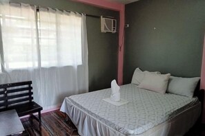 A bedroom with a bed, a bench, and a window with curtains. - Basios Place Tourist Inn by RedDoorz (Palawan)