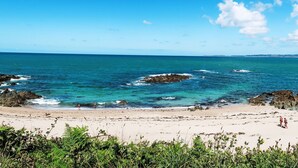 Una playa con agua azul cristalina, afloramientos rocosos y una orilla arenosa.