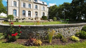 A large, historic stone building with multiple windows and a well-maintained garden in front.
