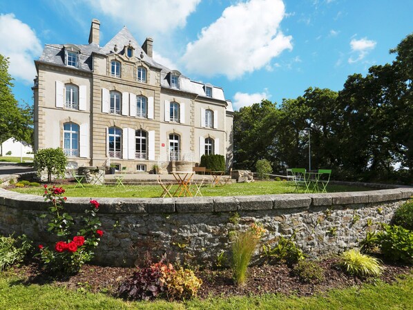 A large, historic stone building with multiple windows and a well-maintained garden in front.