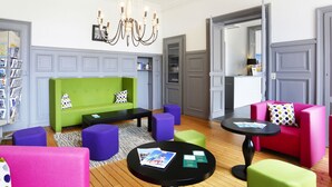 A modern lounge area with a green sofa, purple and pink chairs, and a black table with brochures.