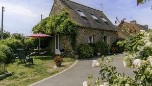 A stone building with a sloped roof, a patio with chairs and a red umbrella, and a garden with flowers and shrubs. - L'Hirondelle by Interhome (Saint Jean du Doigt)