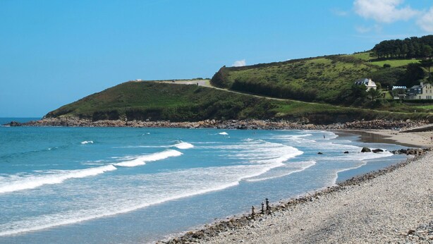 A coastal landscape with a pebbly beach, a clear blue sky, and a hill with buildings. - L'Hirondelle by Interhome (Saint Jean du Doigt)