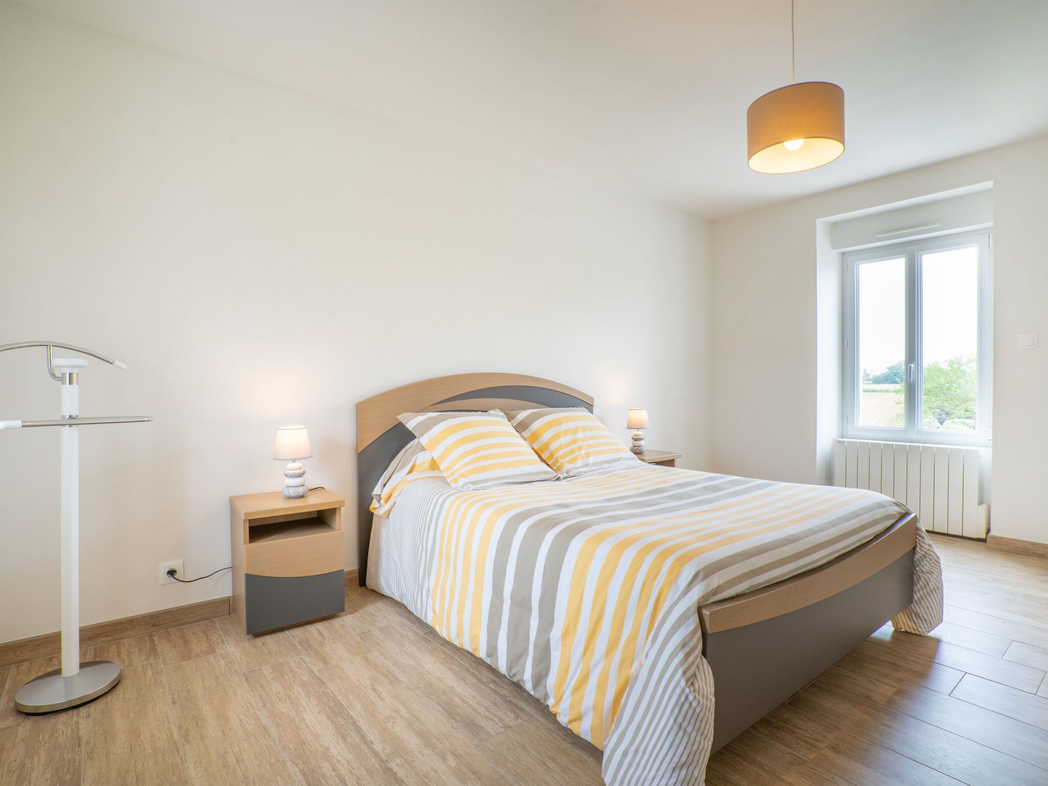 Un dormitorio con una cama, mesitas de noche, una lámpara de pie y una ventana.