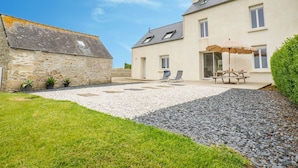A two-story house with a patio area, a stone wall, and a gravel driveway. - L'Oasis by Interhome (Plouneour Trez)