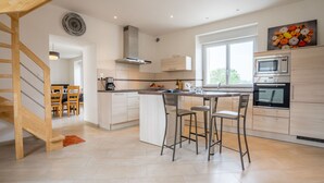 A modern kitchen with a central island, stainless steel appliances, and a dining area with bar stools. - L'Oasis by Interhome (Plouneour Trez)