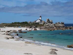 A coastal scene with a lighthouse, rocky outcrops, and a sandy beach.
