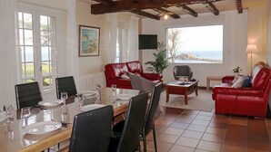 Un comedor con una mesa de madera dispuesta para cuatro personas, un sofá de cuero rojo y vistas al mar a través de amplios ventanales.
