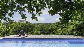 Una piscina con dos sillas de descanso y vista a un área boscosa.