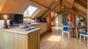Una habitación acogedora tipo buhardilla, con techo de madera, un tragaluz grande, una zona de cocina con estufa, fregadero y una mesa de comedor con sillas.