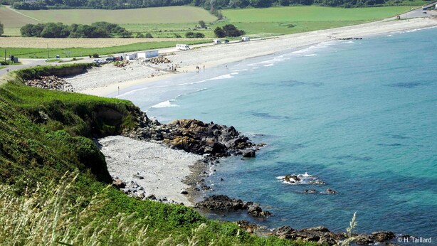 Un paisaje costero con playa, costa rocosa y edificios a lo lejos.