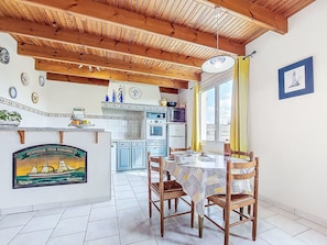 A kitchen with wooden beams, a dining table with chairs, and a wall-mounted clock. - Pors Bae by Interhome (Primelin)