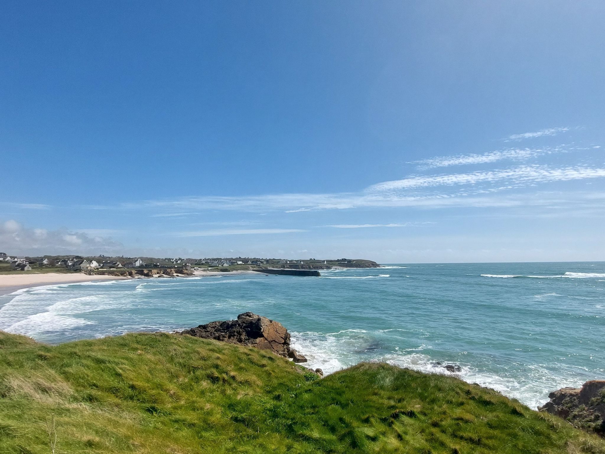 Un paisaje costero con un primer plano herboso, una playa arenosa y un afloramiento rocoso.