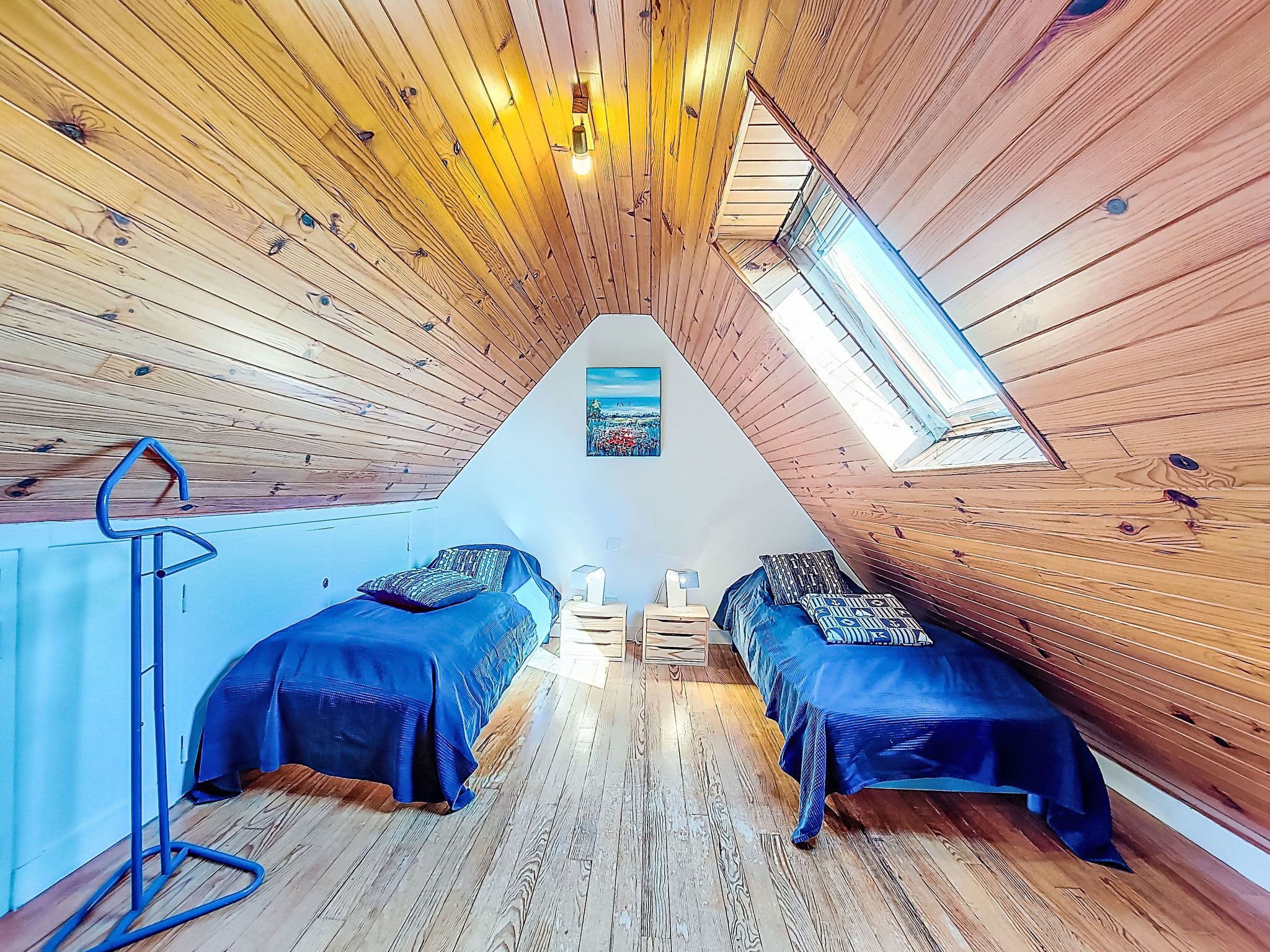 A triangular attic bedroom with wooden walls and a skylight.