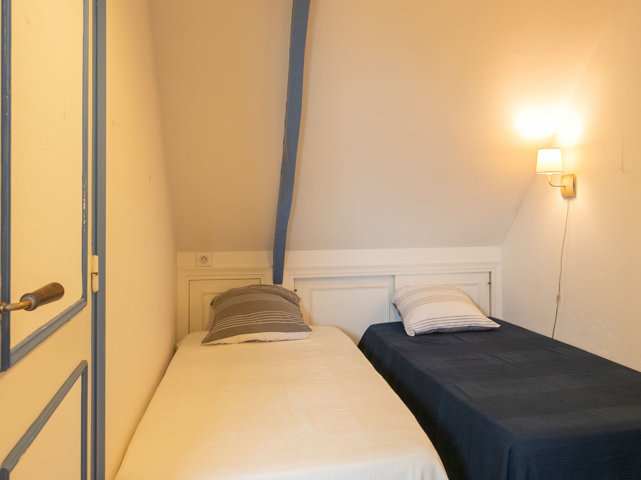 Ett litet, enkelt rum med två sängar, ett sluttande tak och en väggmonterad lampa.