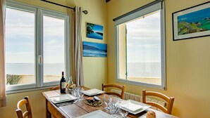 Zona pranzo con tavolo in legno apparecchiata per due, due finestre vista mare e due quadri appesi al muro.