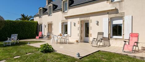 Une maison à deux étages dotée d’un patio, d’un espace salon extérieur et d’un jardin bien entretenu.