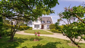 Ein zweistöckiges Haus mit Natursteinfassade, einer Veranda und einem gepflegten Rasen.