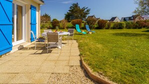 Eine Terrasse mit Tisch und Stühlen, eine blaue Tür und eine Rasenfläche.