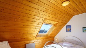 Ein gemütliches Schlafzimmer im Dachgeschoss mit Holzwänden, einem Oberlicht, einem Bett, einem Sessel und einer Heizung.