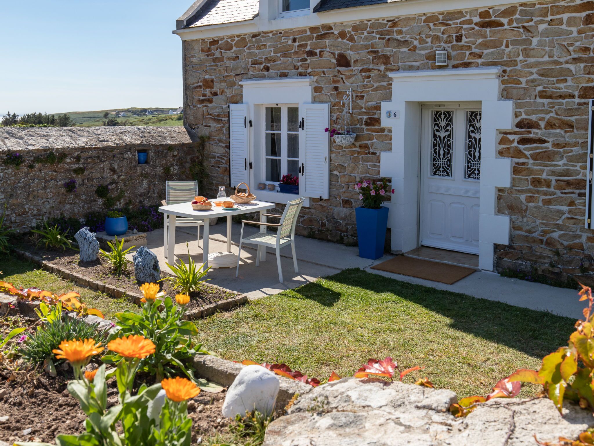 A stone house with a white door, a small garden with flowers, and a table set for two.