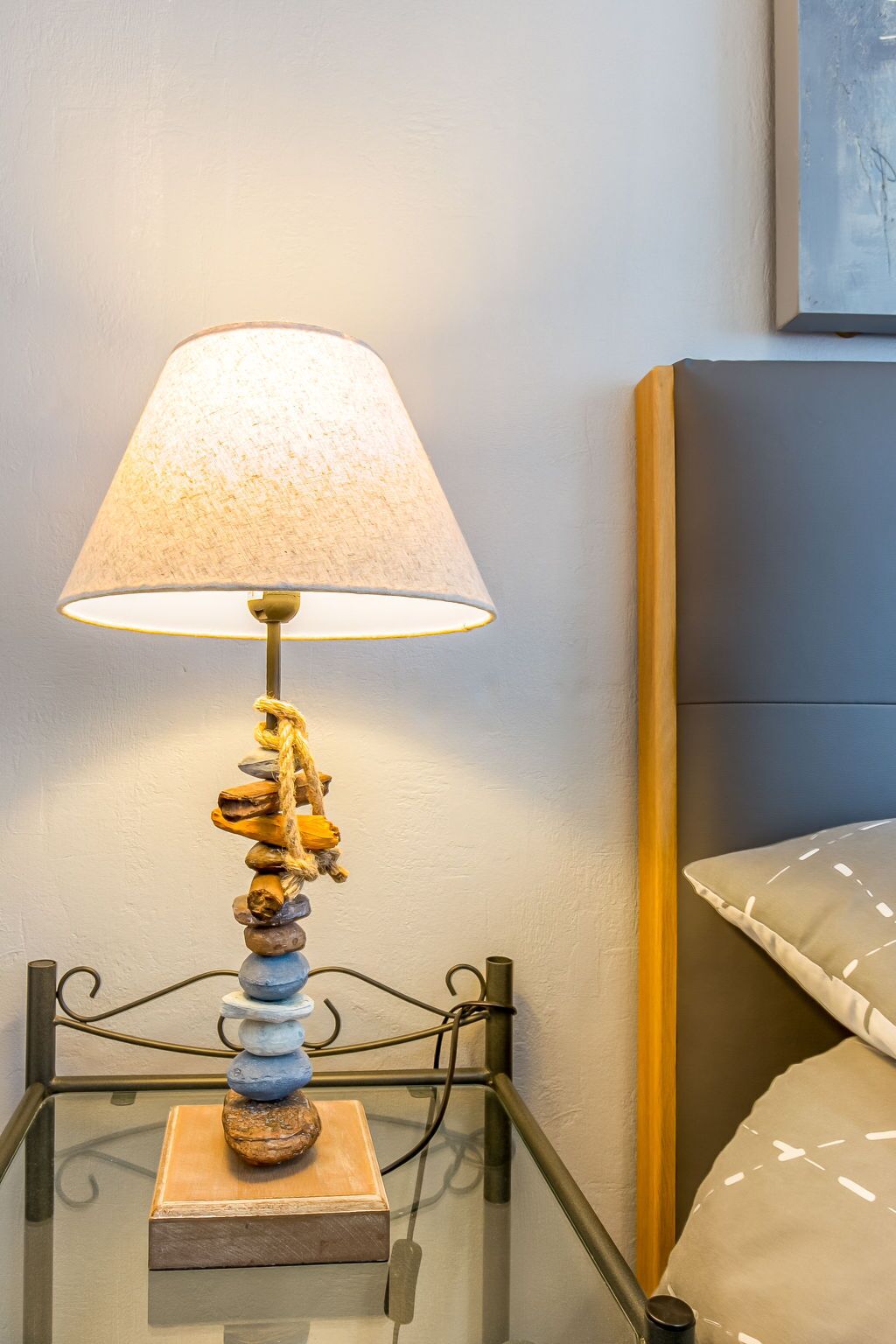 Een nachtkastje met een lamp, een stapel stenen en een bed met hoofdeinde.