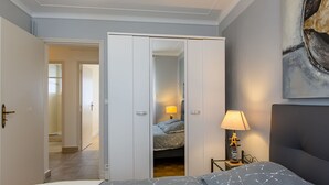 Een slaapkamer met een bed, een kledingkast, een nachtkastje met een lamp en een schilderij aan de muur.