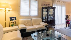 Een woonkamer met een bank, een glazen salontafel met wijnglazen, een kast met servies en een lamp.
