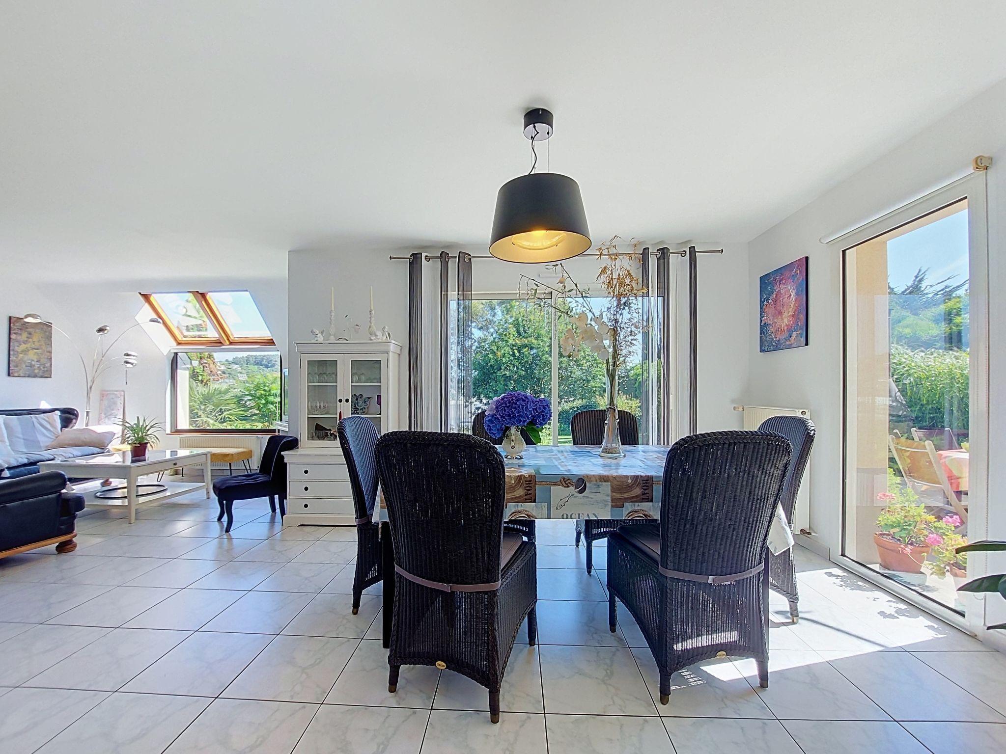A spacious living area with a dining table, chairs, and a large window offering a view of greenery.