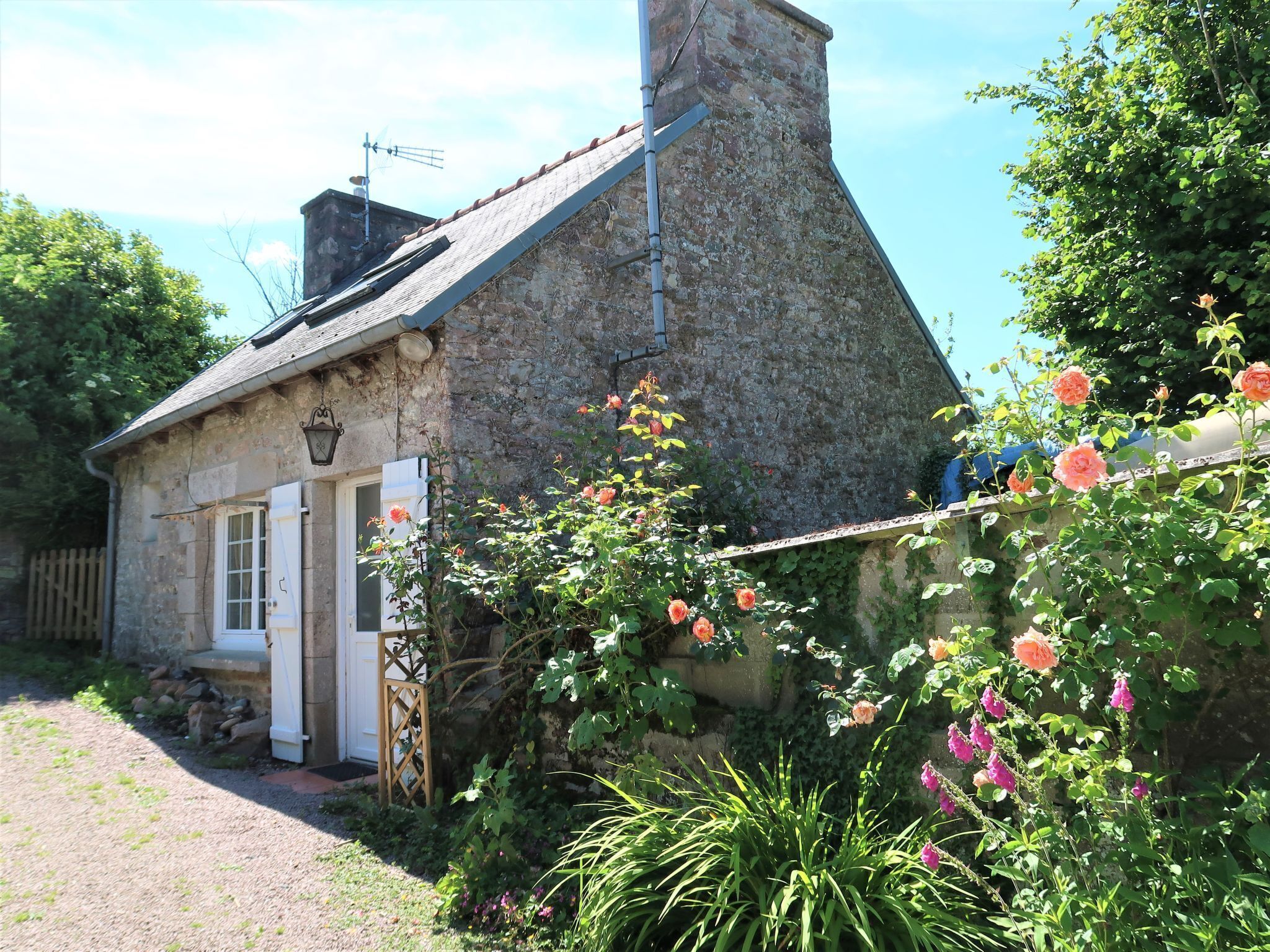 A stone house with a sloped roof, a chimney, and a small garden with flowering plants.
